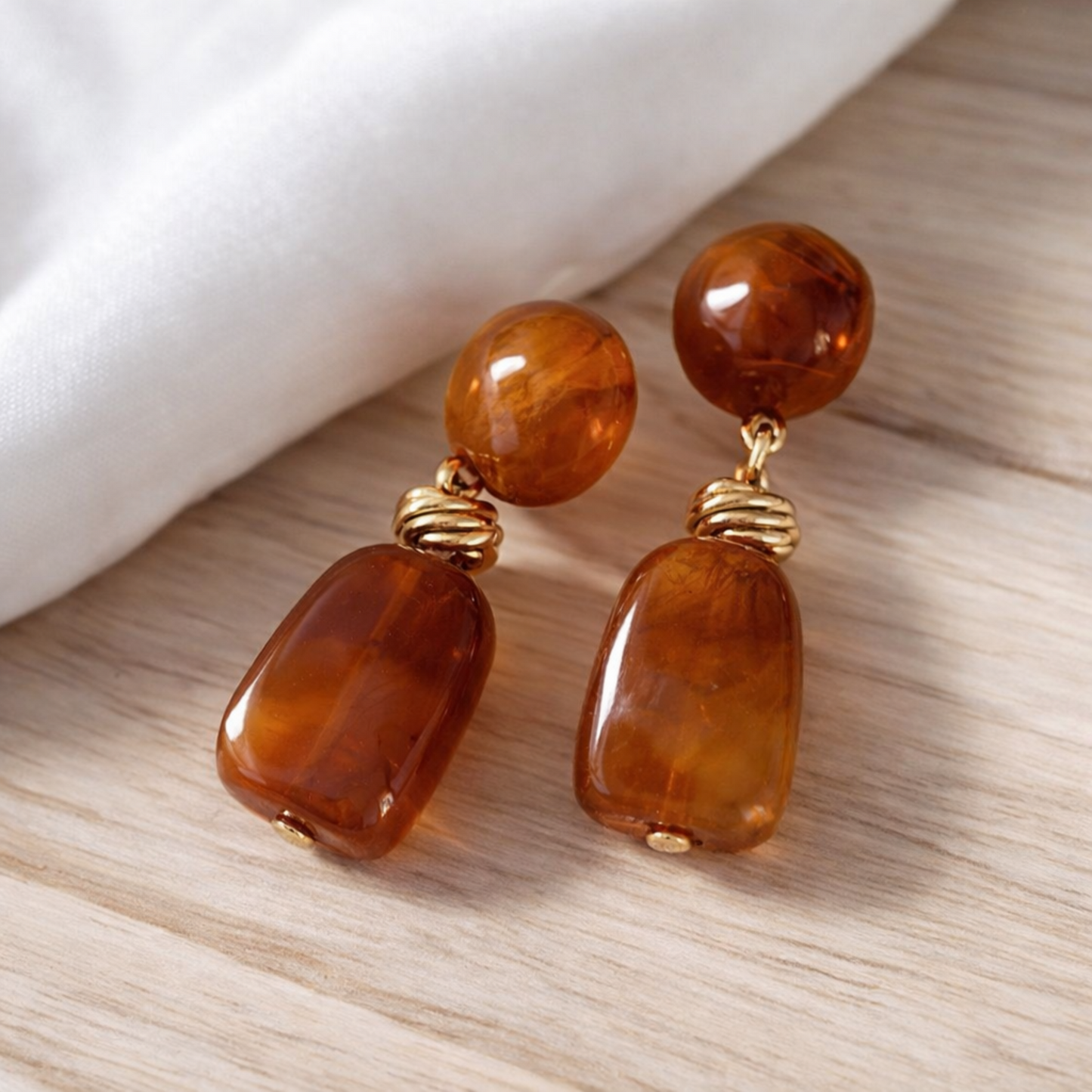 Pair of amber-colored earrings with gold accents on a wooden surface.