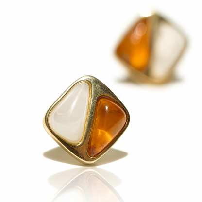 Gold-framed earrings with orange and white stones on a reflective surface.