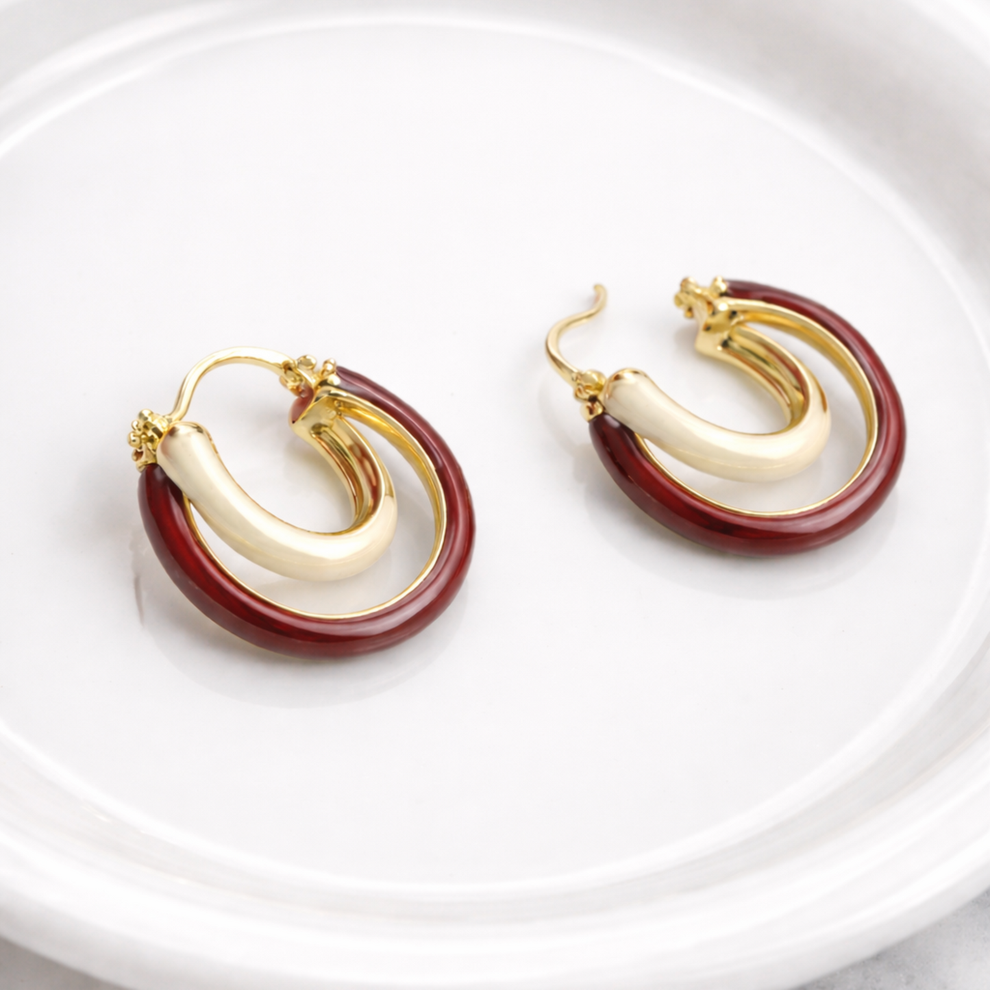 Pair of gold and red hoop earrings on a white plate with a marble background
