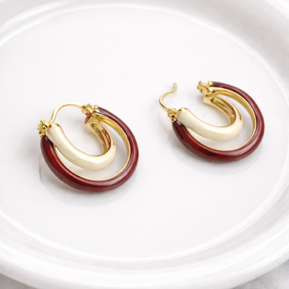 Pair of gold and red hoop earrings on a white plate with a marble background