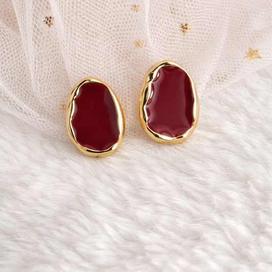 Red earrings with gold frames on a textured white fabric background